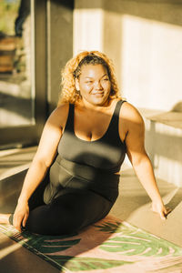 Smiling young woman sitting on exercise mat at retreat center