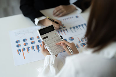 Midsection of businesswoman using calculator while sitting on table