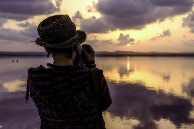 Rear view of man standing on lake against cloudy sky