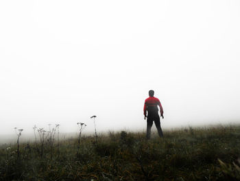 Rear view of man standing on field against sky during foggy weather