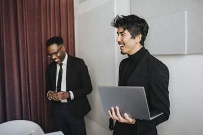 Happy businessman holding laptop by male colleague during meeting at office