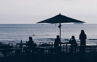 Silhouette people standing by sea against clear sky