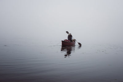 Rear view of woman sitting in boat on river at algonquin provincial park during foggy weather
