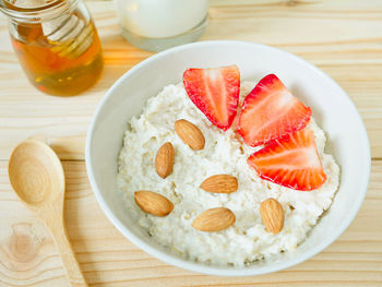 A bowl of oat porridge topped with almonds and fresh strawberries served with milk and honey.
