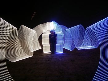 Young man standing amidst light painting on field at night