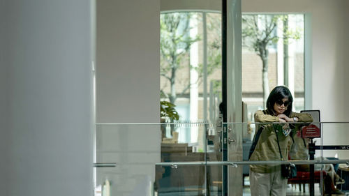 Woman using phone while standing on window