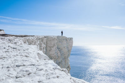 Man standing on rock by sea against sky