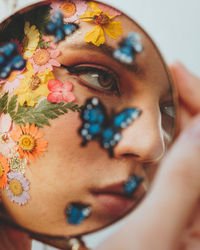 Beautiful young woman with flowers on face seen in mirror