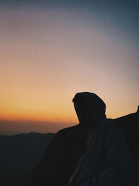 Silhouette man sitting on mountain against sky during sunset
