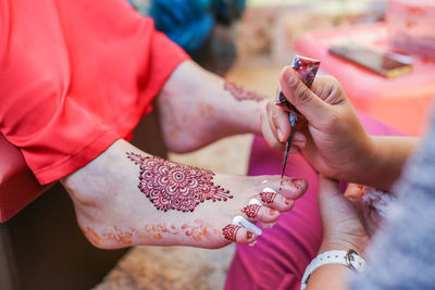 Cropped image of beautician making henna tattoo on bride leg