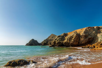 Scenic view of rock formation by sea against clear blue sky