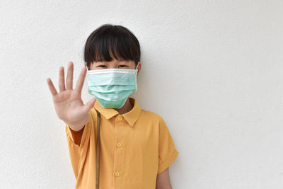 Portrait of girl wearing mask gesturing against wall