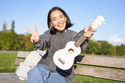 Portrait of young woman with guitar while standing against sky