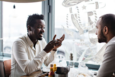 Smiling young male friends talking while having brunch at restaurant