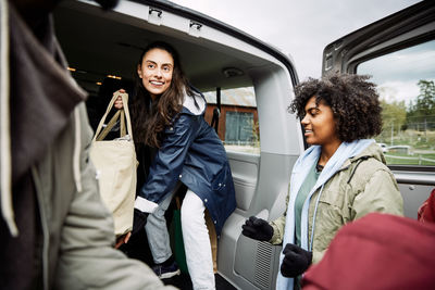 Smiling female passing bag to friends while standing in car