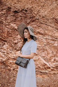 Young woman looking away while standing against rock formation