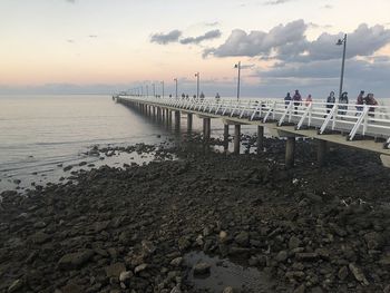 Pier on beach against sky during sunset