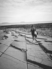 Rear view of woman walking at beach against sky