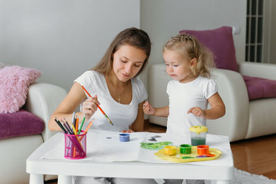 Mother and toddler daughter painting at home. happy creative family with child spending time