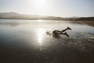 Carefree man jumping into lake against clear sky during sunny day