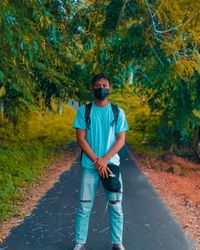 Portrait of young man standing on road against trees