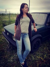 Young woman standing by car against sky