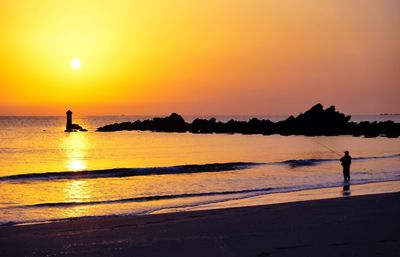 Silhouette man fishing in sea against sky during sunset