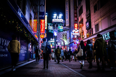 People walking on city street amidst illuminated buildings