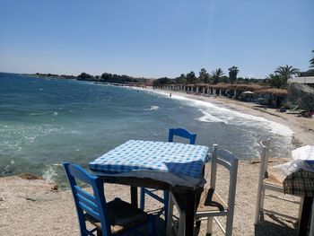 Chairs and tables on beach against clear blue sky