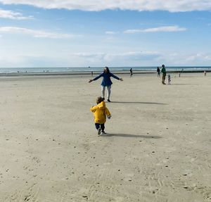 Rear view of child running on the beach against sky