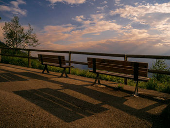 Empty bench by railing against sky during sunset