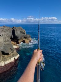 Man fishing on rock by sea against sky