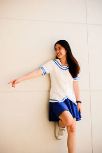 Smiling young woman pointing while looking away against wall