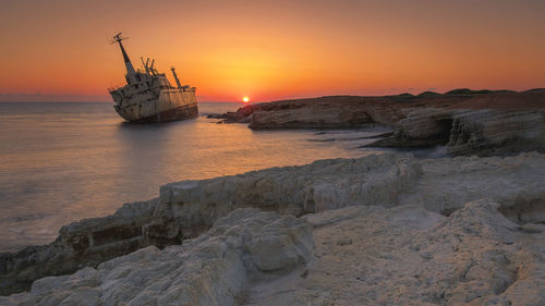 Sailboat on sea shore against sky during sunset