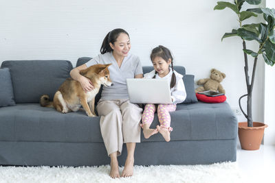 Smiling mother and daughter using laptop while sitting with dog on sofa