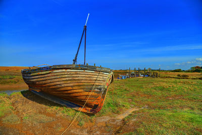 Abandoned boat moored on field against sky