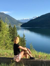 Woman sitting by lake against sky