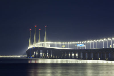 Illuminated city by sea against sky at night