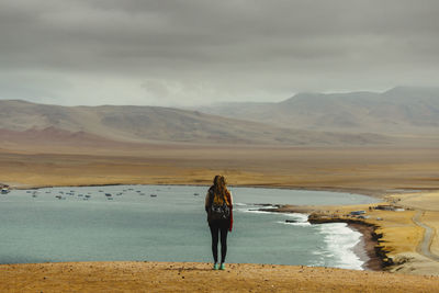Rear view of woman looking at lake against cloudy sky