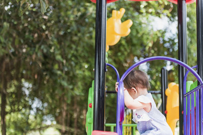 A little girl alone stood on the stairs at the top of the slide. back view.