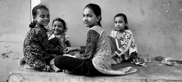 Portrait of friends sitting on floor against wall