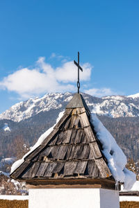 The mountain chapel with cross covered with wooden shingle. snow-capped mountains, blue sky