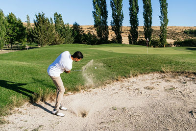 Male player hitting ball while standing in hazard area of golf course in countryside