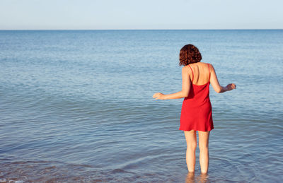 Rear view of woman standing in sea water against sky