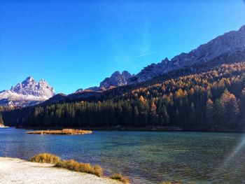 Scenic view of lake by mountains against clear blue sky