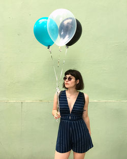 Young woman with balloon standing against blue wall