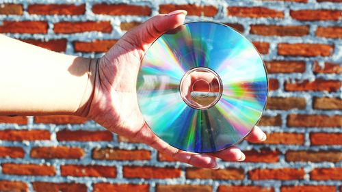 Cropped hand of woman holding compact disc against brick wall