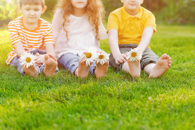 Children feet with daisy flower on green grass in a summer park.