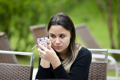 Portrait of young woman holding camera outdoors