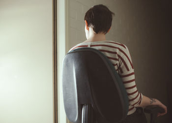 Rear view of person sitting on chair by glass window